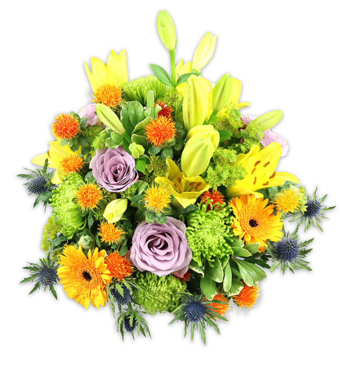 Presented on a clean white surface, this full-bodied floral composition reads as a lively hymn to colour and texture: dominant warm yellows and oranges dance around cooler lavender and steely-blue accents, all held together by rich green foliage. Prominent yellow Asiatic lilies rise above the mound, some unfurled to reveal speckled throats and slender stamens, others retained as graceful buds that add verticality and a sense of unfolding promise. Two soft lavender roses sit slightly recessed near the centre, their velvety spirals offering a calm focal point amid the exuberant hues. Scattered through the arrangement are vivid orange Gerbera daisies, their broad ray-like petals fanning from darker centres and drawing the eye with immediate cheer.
Clusters of lime-green cushion chrysanthemums provide plush, textured massing that gives the bouquet a generous, almost tapestry-like density, while smaller spherical accents in bright orange and golden yellow introduce lively, prickly highlights. The cool indigo-blue Eryngium thistles emerge along the lower and lateral edges, their sharply formed bracts introducing an architectural, almost sculptural counterbalance to the softer blooms. A variety of leaves - glossy, matte, broad and narrow - build depth and shelter the flowers, catching the soft studio light to reveal subtle sheen and shadow.
This arrangement, with its celebratory warmth and thoughtful contrasts, feels at home in neighbourhood settings from the terraces near Vauxhall Bridge to riverside apartments along the Albert Embankment. It conveys joy, gratitude, or gentle sympathy with an assured, modern floral voice and would make a striking centrepiece or a thoughtful gift locally.